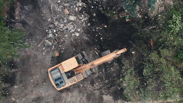 Aerial top view of yellow excavator at construction site after demolition of house.