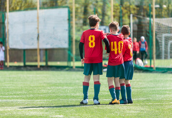 Young sport boys in red sportswear running and kicking a ball on pitch. Soccer youth team plays football in summer. Activities for kids, training