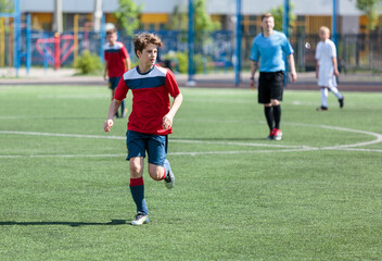 Obraz premium Teenager in red sportswear plays football on field, dribbles ball. Young soccer players with ball on green grass. Training, active lifestyle 