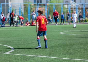 Obraz premium Teenager in red sportswear plays football on field, dribbles ball. Young soccer players with ball on green grass. Training, active lifestyle 