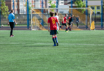 Obraz premium Young sport boys in red sportswear running and kicking a ball on pitch. Soccer youth team plays football in summer. Activities for kids, training