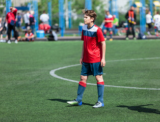 Obraz premium Teenager in red sportswear plays football on field, dribbles ball. Young soccer players with ball on green grass. Training, active lifestyle 