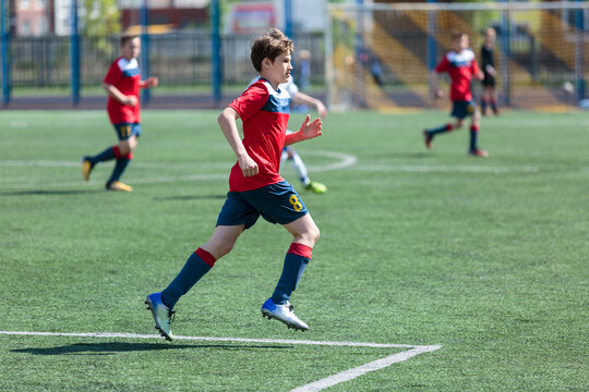 Teenager in red sportswear plays football on field, dribbles ball. Young soccer players with ball on green grass. Training, active lifestyle 