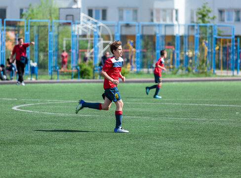 Teenager in red sportswear plays football on field, dribbles ball. Young soccer players with ball on green grass. Training, active lifestyle 