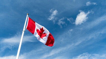 Canada flag pole waving in the wind under beautiful blue sky and clouds wallpaper. Canadian national red maple leaf symbol background