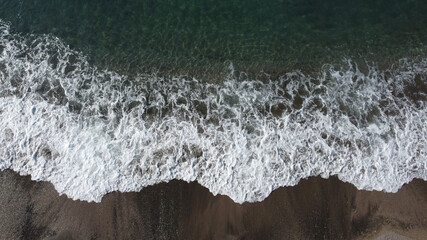 Aerial shot of waves splashing on sandy shore