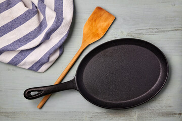 An oval cast iron frying pan with a wooden spatula and a tea towel