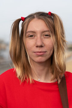 Vertical portrait of pretty young blonde woman with a soulful and intense look, freckles on her face and two funny ponytails on head, front view. Precocious female teenager.