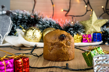 Mini Panettone on wooden table with Christmas decorations. Red, silver and gold balls, gift boxes, lights, Christmas tree and others. Selective focus.