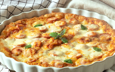 pizza with sausages, basil and cheese in a white dish