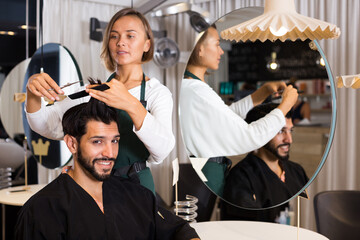 Fototapeta na wymiar adult hairdresser working with scissors and comb with smiling man