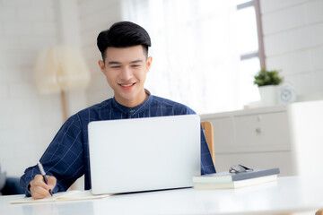 Fototapeta premium Young asian business man writing on notebook for planning working and using laptop computer on desk at home, notes about finance, male study and learning, business and communication concept.