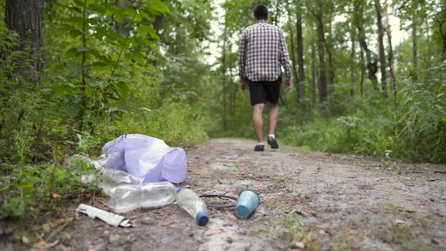 A bad man throws garbage out of a plastic trash bag in the forest. The male intruder leaves litter trash and walks away. Pollution and ecological problem, plastic recycling, pollution of nature.