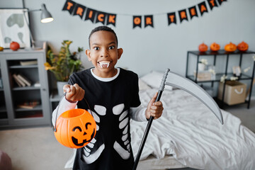 Waist up portrait of teenage African-American boy holding Halloween bucket while making faces at...