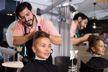 positive man hairdresser making hairstyle for woman in salon.