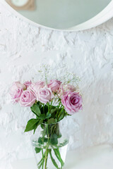 a bouquet of light pink roses against a white wall and part of a round mirror