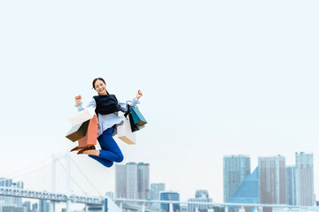 買い物袋を沢山持ってジャンプする女性（セール・爆買い）