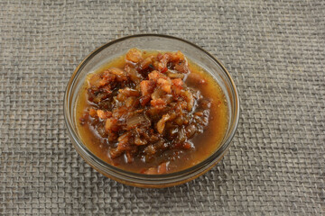 Red wine sauce with bacon and chopped shallot on glass ingredient bowl on gray burlap