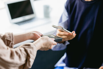 カフェ（コワーキングスペース）でスマホ決済をする女性