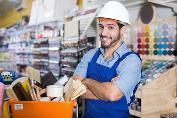 Satisfied foreman standing crossed hands near basket with tools in hardware shop