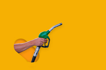 Man holds a refueling gun in his hand for refueling cars isolated on yellow background. Gas station with diesel and gasoline fuel close-up. - obrazy, fototapety, plakaty