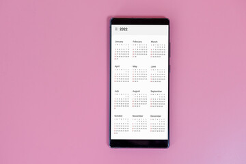 Black smart phone show calendar App 2022 on pink background. New Year Concept.