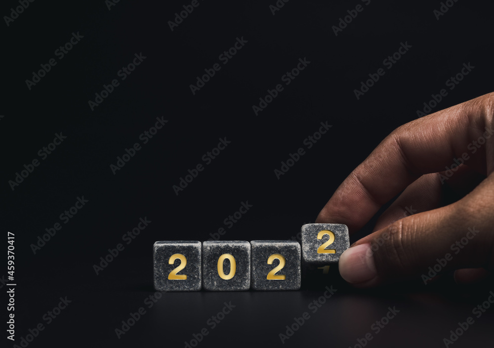 Poster the year 2021 change to 2022 with the successful concept. close-up hand flipping black cube blocks f
