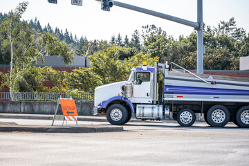 Powerful tip truck with covered trailer running on the city street crossroad with traffic light and detour road sign