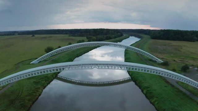 Flying above gas pipes running across calm river Morava in Slovakia. Aerial sunset footage of two parallel bridges connecting both river banks.