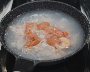 Fresh raw chicken is boiled in a metal pan for cooking.