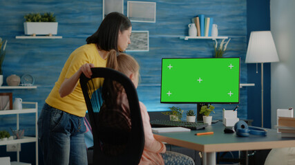 Mother and pupil doing homework with horizontal green screen on computer at desk. Child and parent...