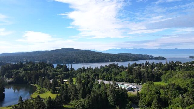Aerial footage of pacific ocean views and peninsulas with rainforests on Vancouver Island. Slowly lowering camera movement revealing old bridge over river.