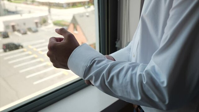man in white dress shirt adjusting his cuff sleeve by the window during daytime