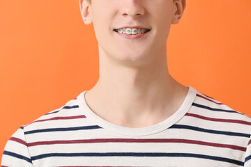 Handsome man with dental braces on color background, closeup