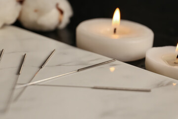 Board with acupuncture needles and aroma candles on dark background, closeup