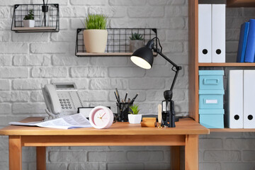 Comfortable workplace with alarm clock and lamp in office