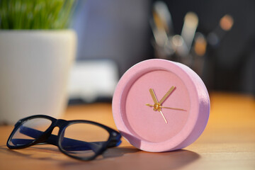 Alarm clock and eyeglasses on table in office, closeup