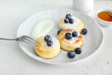 Plate with tasty cottage cheese pancakes, blueberry and sour cream on table