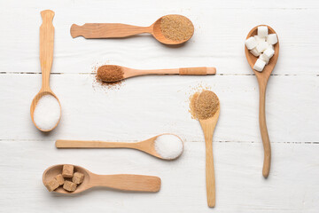 Spoons with sugar on white wooden background
