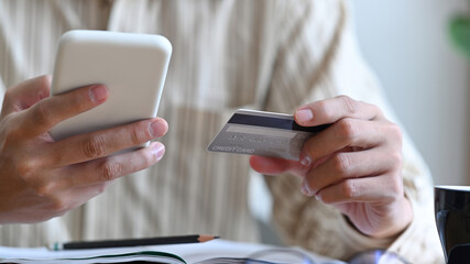 Cropped shot male holding credit card and payment online on smart phone.