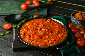 Frying pan with delicious chili con carne and tomatoes on dark wooden background