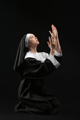 Young praying nun on dark background