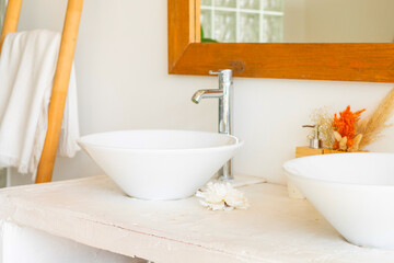 stylish and modern design bathroom interior with two white sinks, wicker baskets for cosmetics, mirror in wooden frame, dried flowers in vases, home plants in pot in Balinese style with white walls