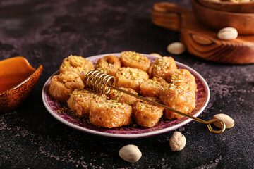 Plate with delicious baklava and honey dipper stick on dark background