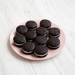 Homemade Oreos on a pink plate on a white wooden background, side view.