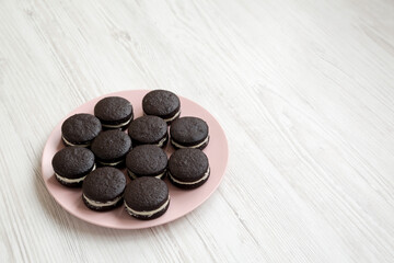 Homemade Oreos on a pink plate on a white wooden surface, side view. Copy space.