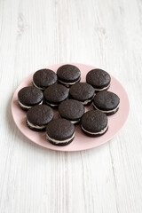 Homemade Oreos on a pink plate on a white wooden background, low angle view.