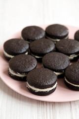 Homemade Oreos on a pink plate on a white wooden background, low angle view.