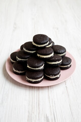 Homemade Oreos on a pink plate on a white wooden background, side view.