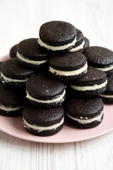 Homemade Oreos on a pink plate on a white wooden surface, low angle view.